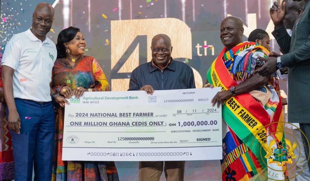 President Akufo-Addo ( middle) being assisted by other dignitaries to present the 2024 overall National Best Farmer dummy cheque to Nana Owusu Achiaw (right). Photo Victor A. Buxton