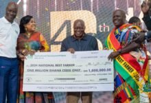 President Akufo-Addo ( middle) being assisted by other dignitaries to present the 2024 overall National Best Farmer dummy cheque to Nana Owusu Achiaw (right). Photo Victor A. Buxton