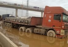 A truck stucked in a muddy pool of water in the middle of the road