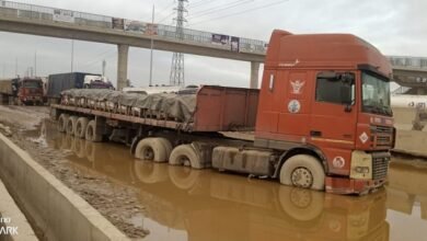 A truck stucked in a muddy pool of water in the middle of the road