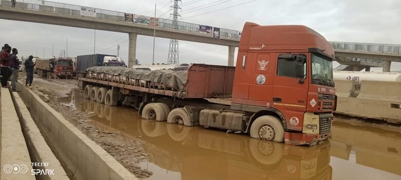 A truck stucked in a muddy pool of water in the middle of the road