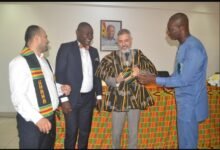 • Mr Anyetei (right) assisting Mr Gungor to wear a hat after presenting a smock to him during the visit. With them is Mr Emmanuel Nyako Baah (second from left)