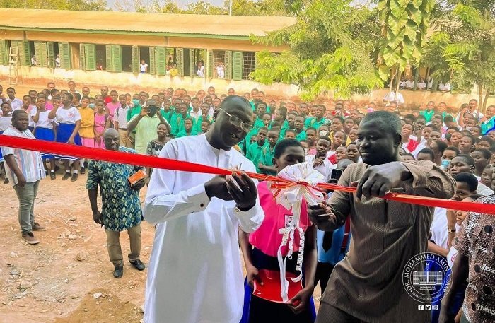 Dr Mohammed Amin Adam being assisted by Mr Abukari Yakubu to cut the tape to officially open the block
