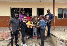 Mrs Addo presenting the cash to Ataa Lartey. Looking on are the husband of the donour, Mr Addo (left) and staff and children of the Academy