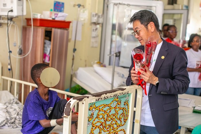 Mr. Li presenting chocolate and a flower to a patient in the children's ward.