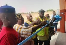 Mr Ndebilla (right) being assisted by Mr Ayamwego and others to cut the tape to inaugurate the classroom block