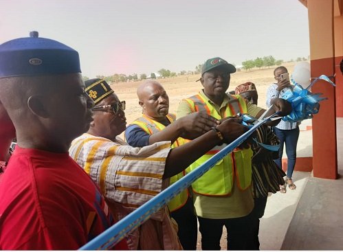Mr Ndebilla (right) being assisted by Mr Ayamwego and others to cut the tape to inaugurate the classroom block