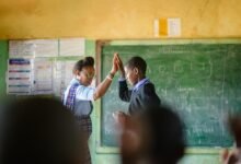 African Schoolboy high five interchange teacher in the front of the class. The image is taken from the back of the classroom through the rear view of the other learners defocussed. Malealea Lesotho