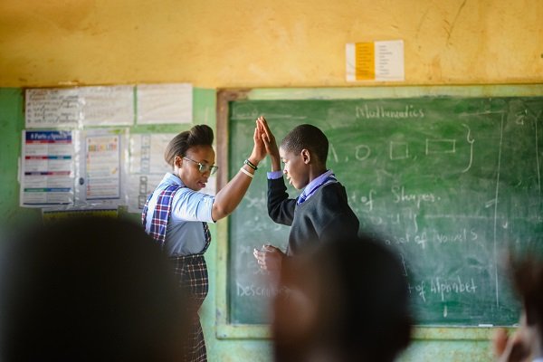 African Schoolboy high five interchange teacher in the front of the class. The image is taken from the back of the classroom through the rear view of the other learners defocussed. Malealea Lesotho