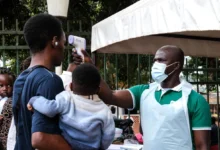 A health official uses a thermometer to screen people in front of a hospital