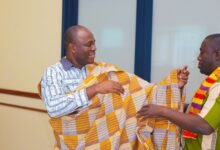 A man being shown how to put on the Kente