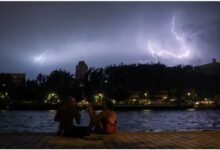 People sit on the banks of the Bassin de la Villette during a storm, as lightning strikes behind them amid a heatwave in Paris