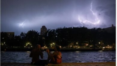 People sit on the banks of the Bassin de la Villette during a storm, as lightning strikes behind them amid a heatwave in Paris