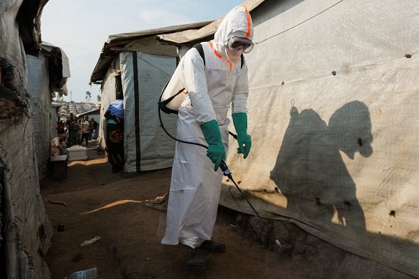 A health worker in full personal protective equipment (PPE) disinfects an area while preparing for the burial of suspected Ebola victims in DR Congo