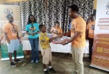 A beneficiary student receiving a backpack from Mr Laryea