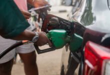 A customer stands near an attendant filling up his car at a filling station, as fuel costs rise in Abuja, Nigeria