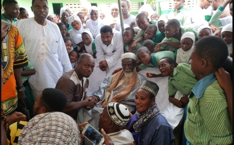 Mr Issah in a handshake with Sheikh Dr Osman Nuhu Sharubutu during their meeting. With them are pupils from AFRAMISCO