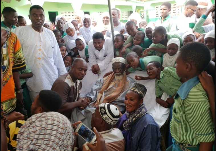 Mr Issah in a handshake with Sheikh Dr Osman Nuhu Sharubutu during their meeting. With them are pupils from AFRAMISCO