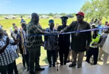 (in set) Mr Kuuire (in cap) being assisted by ASP Banafo and Mr Ziniel (second from left) to cut the tape to open the Police Post at Kokoligu