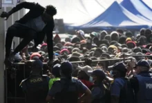 A Malawian migrant jumps over a barricade as the police officer manage the queue for their deportation at a temporary centre, in Durban