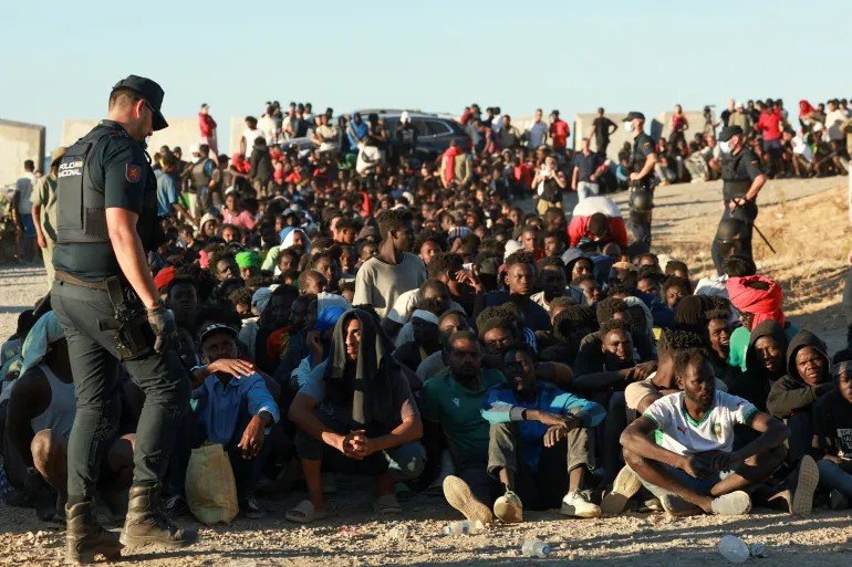 Migrants and asylum seekers wait in line to receive food and drink from the Red Cross in Ceut, Spain