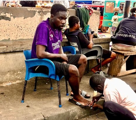 A traditional nail cutter attending to a client at a trotro station